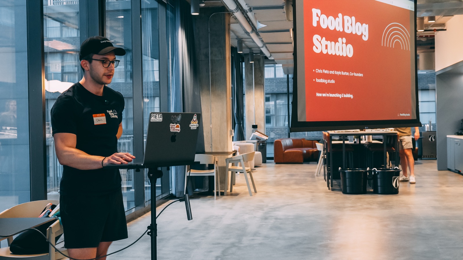 Chris Pieta presenting Food Blog Studio from a laptop, with the title slide on a projector screen behind him